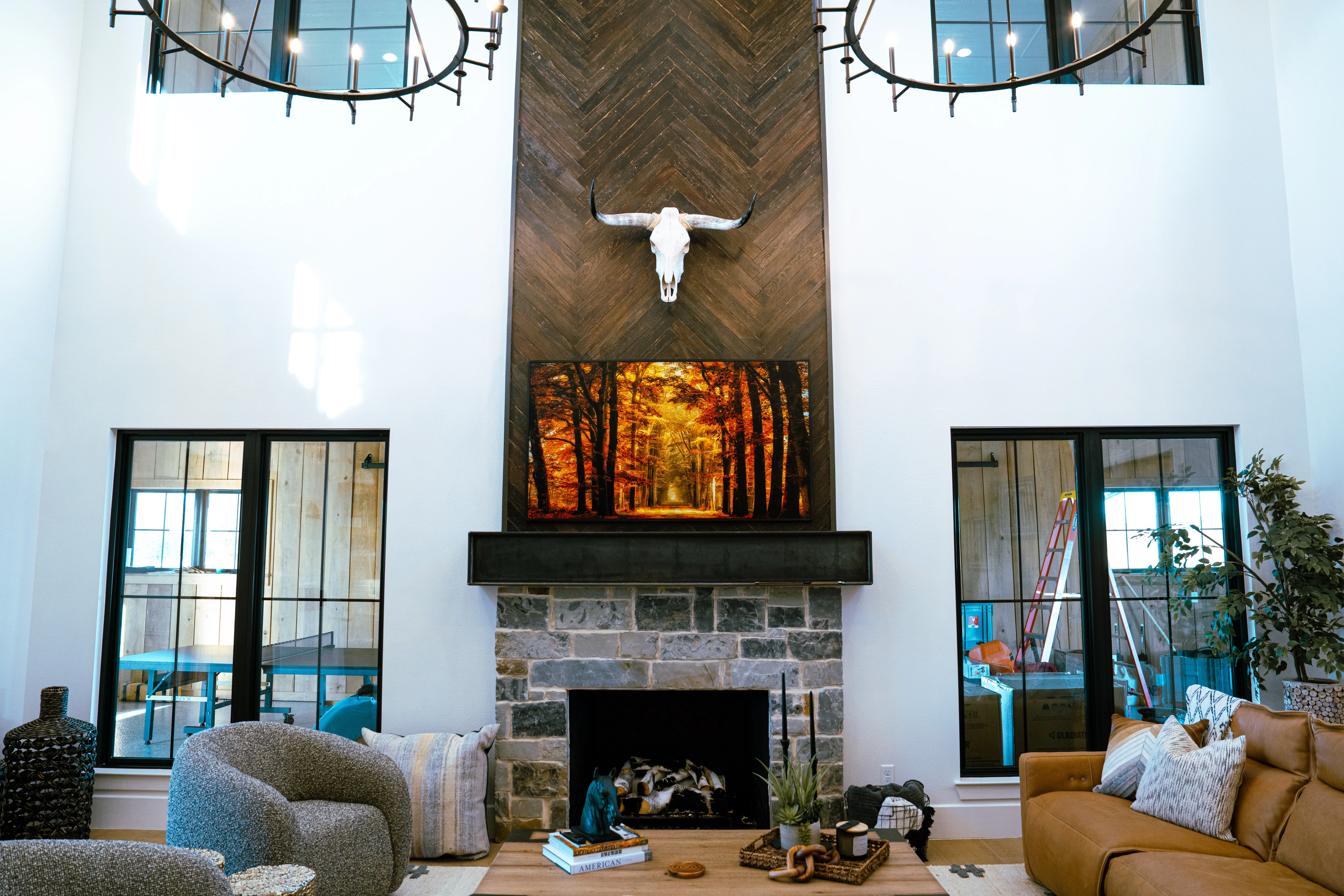 Two-story great room with a stone fireplace, herringbone wood chimney, and a mounted longhorn skull in a Harrill Construction custom home, photographed by Grit Blueprint