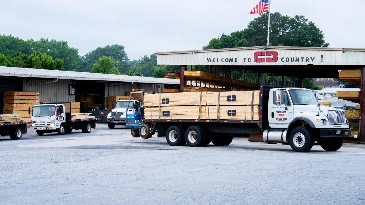 Cofer Bros. flatbed trucks loaded with lumber under the Welcome To CB Country canopy in Tucker, Georgia, photographed by Grit Blueprint