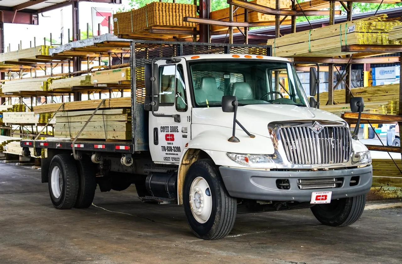 Cofer Bros. delivery truck parked beside towering racks of dimensional lumber in the yard, photographed by Grit Blueprint