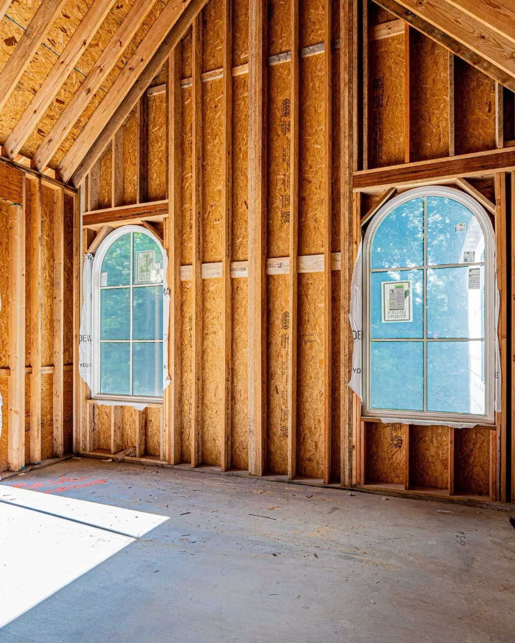 Framed interior with two arched grid windows and exposed wall studs in a Madewell Homes build, windows supplied by Magbee Contractors Supply, photographed by Grit Blueprint