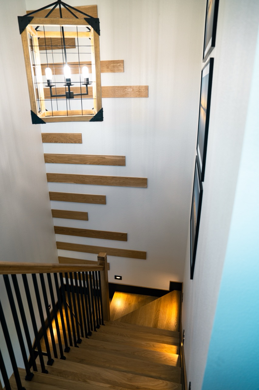 Tall stairwell with a cascading plank feature wall and an iron lantern chandelier, photographed by Grit Blueprint