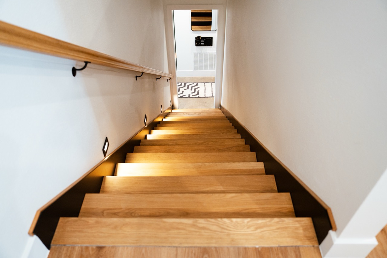 White-oak staircase descending a lit hallway to the entry, stair package by Coffman Stair Parts, photographed by Grit Blueprint
