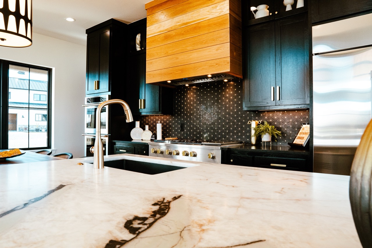 Open kitchen with deep-green cabinetry, a quartzite waterfall island, and a wood range hood, photographed by Grit Blueprint