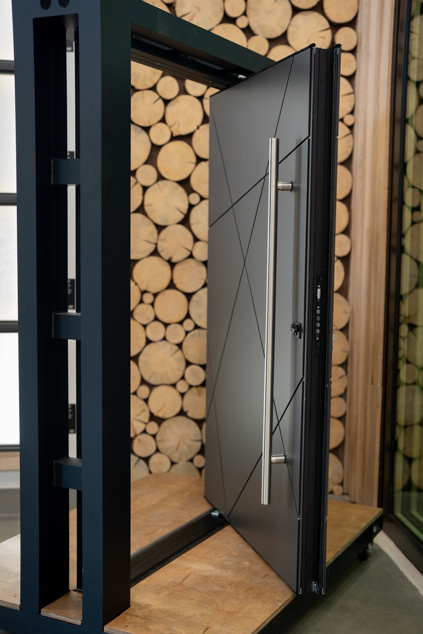 Modern black pivot security entry door displayed against a stacked-log wall, photographed by Grit Blueprint