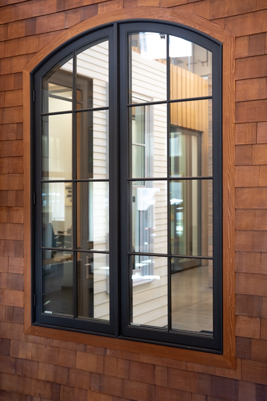 Arched black-framed casement window set in a cedar-shingle wall, photographed by Grit Blueprint