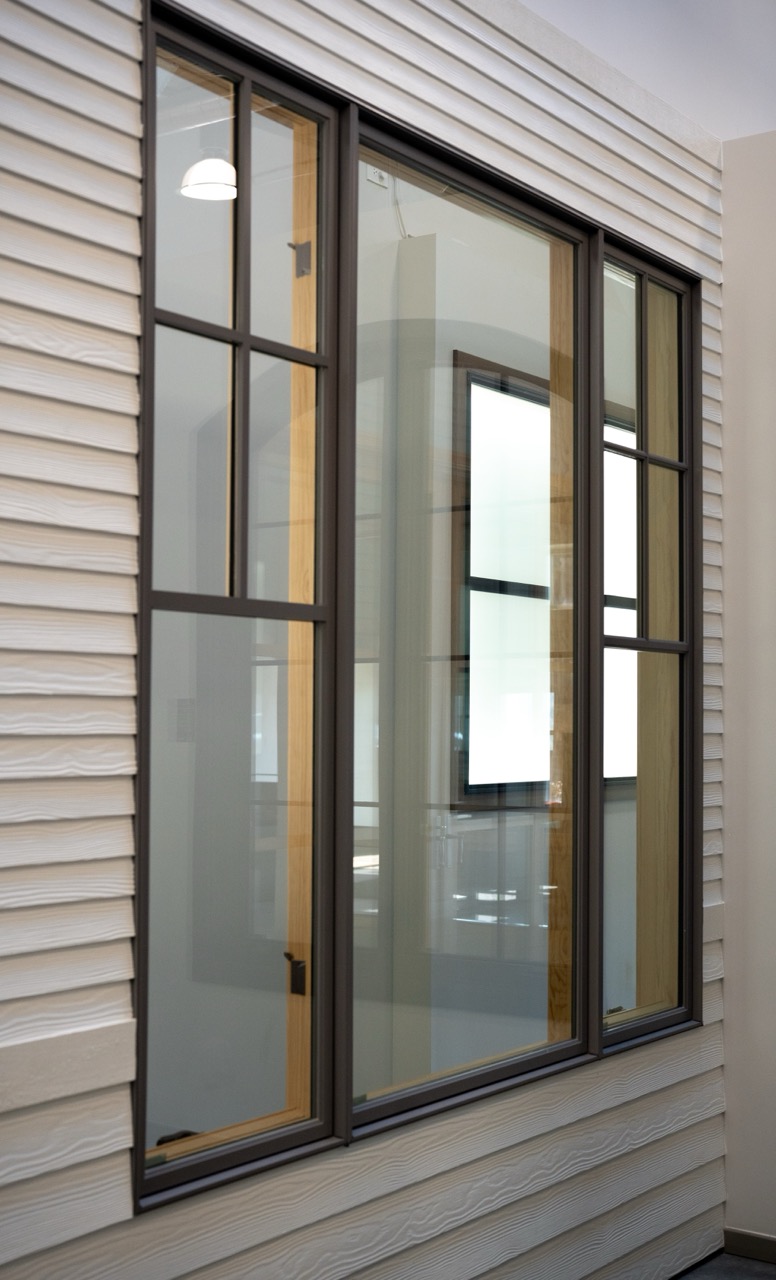 Bronze-framed three-panel window set in white lap siding, photographed by Grit Blueprint