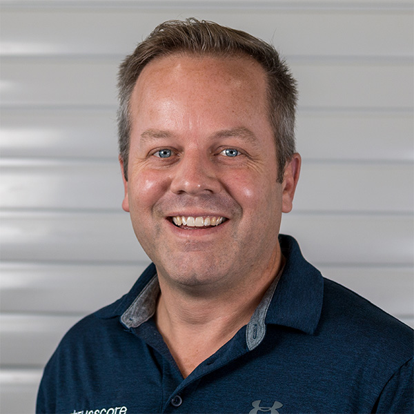 Headshot of a smiling man in a navy Trusscore polo shirt in front of a light gray panel wall.