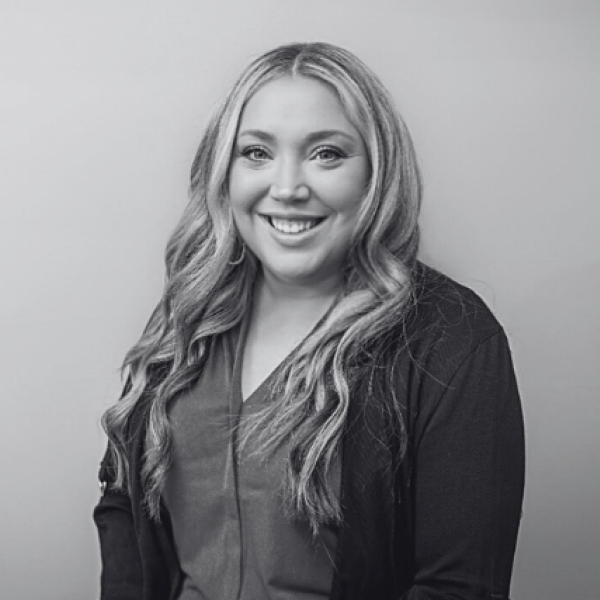 Black and white portrait of a smiling woman with long wavy hair and a dark cardigan against a plain backdrop.
