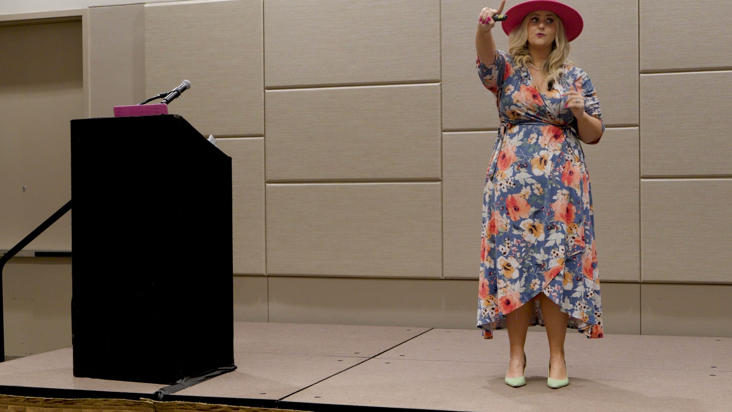 Stefanie Couch raising one hand while presenting on a stage beside a black podium