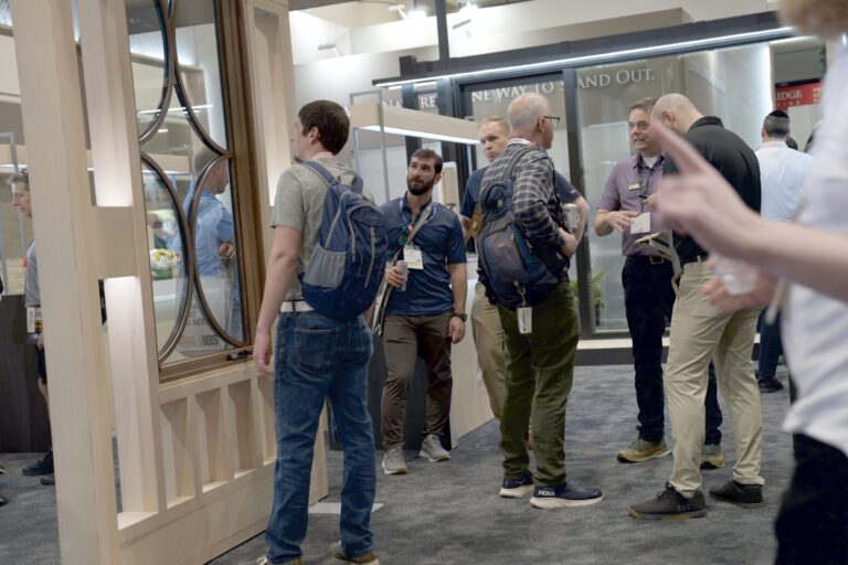 People with show badges standing beside window displays in the booth