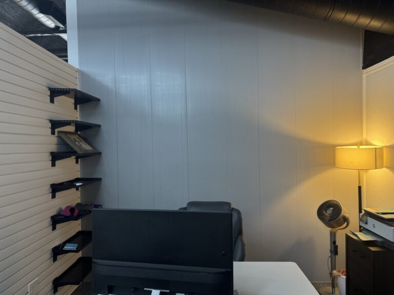 Trusscore gray wall panels behind a desk, with shelves mounted on a white slat wall to the left
