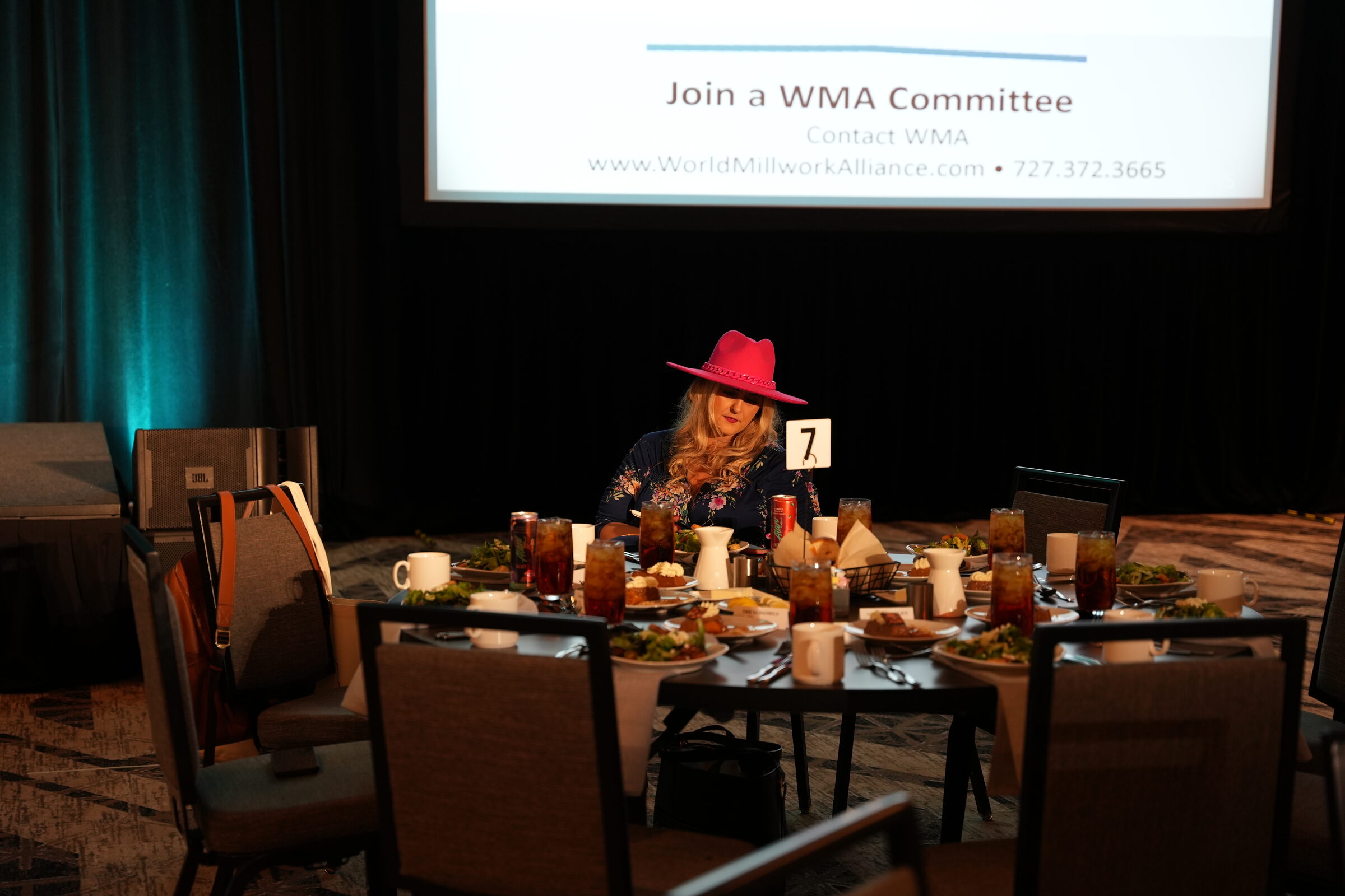 Stefanie Couch in a pink hat seated at a round table marked 7 in a darkened ballroom