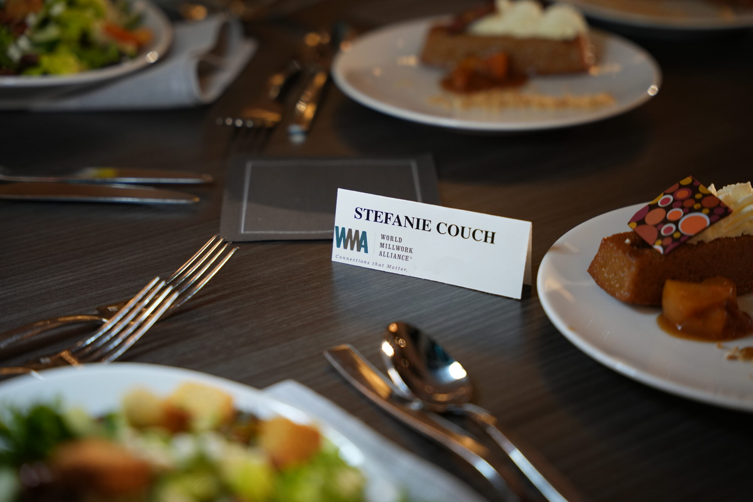A Stefanie Couch place card with the World Millwork Alliance logo on a set lunch table
