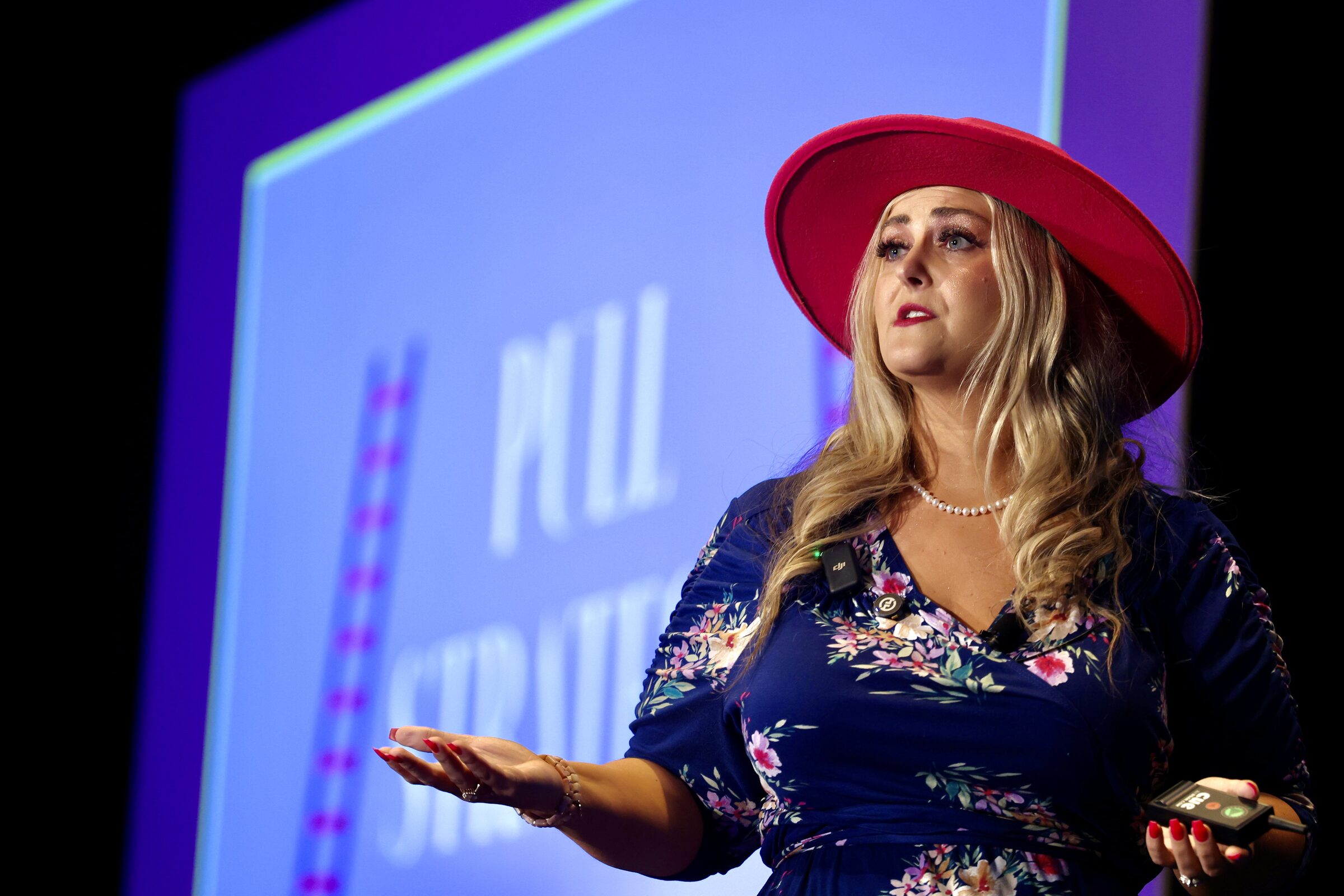 Close view of Stefanie Couch gesturing as she speaks, with a purple presentation slide behind her